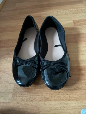 Svarta lackade ballerinaskor med rosett - Stilrena svarta ballerinaskor i glansigt lackmaterial med söt rosettdetalj framtill. Rund tå och mjuk innersula för extra komfort. Perfekta för dig som gillar en klassisk och enkel look. Säljer dessa för att de är för små (har storlek 40). Ballerinaskorna har lite repor men de är inget man ser ifall man inte kollar noggrant🙌