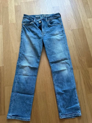 Blå straight fit jeans med stretch - Säljer ett par blå jeans med regular straight fit och stretch. Jeansen har klassisk femficksdesign, ljusa slitningar och är tillverkade i denim. Perfekta för en avslappnad och stilren look.