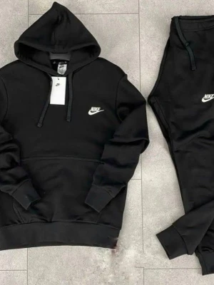 Svart Nike loungewear set - Snyggt svart loungewear set från Nike med hoodie och matchande byxor. Hoodien har dragsko i huvan, magficka och Nike-logga på bröstet. Byxorna har resår i midjan och Nike-logga på benet. Perfekt för chill dagar hemma.