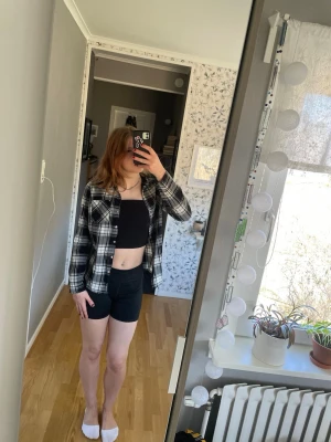 Svartvit rutig skjorta - Säljer en svartvit rutig skjorta med klassisk krage och knappar framtill. Skjortan har lång ärm och en avslappnad passform, perfekt att bära öppen eller stängd. Materialet känns mjukt och bekvämt, material är en bomullsblandning och väldigt tunt 