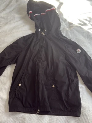 Svart Moncler vindjacka med huva - Svart vindjacka från Moncler med huva och dragkedja. Jackan har två fickor med tryckknappar och Moncler-logga på ärmen. Den är XS men kan passa S också. Pris kan diskuteras👍