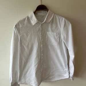 Vit skjorta från Lindex - Klassisk vit skjorta från Lindex med lång ärm och bröstficka. Skjortan har knappar framtill och en stilren krage. Perfekt för en clean och enkel look.