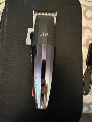 JRL svart och silver hårtrimmer - Elektrisk hårtrimmer från JRL i svart och silver med digital display. Ergonomisk design med metallspak på sidan för justering av klipplängd. Perfekt för styling och trimning av hår och skägg. Tillverkad i plast och metall. Från 05= 1,5mm till 8=25mm 