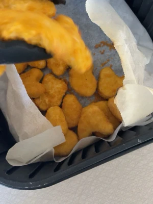 Krispiga kycklingnuggets - Ett gäng gyllene kycklingnuggets med frasig panering, perfekta att dippa eller äta som snacks. Nuggetsarna har en klassisk form och är lagda på bakplåtspapper i en svart form. Passar till både lunch och mellanmål.