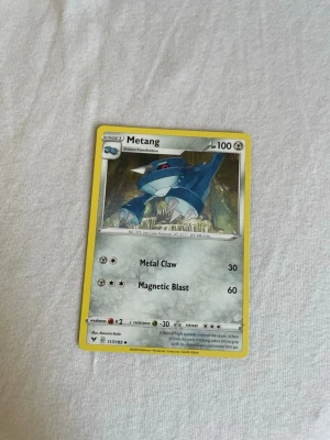 Pokémonkort Metang 117/185 - Samlarobjekt! Pokémonkortet Metang 117/185 från Sword & Shield-serien. Kortet har gul ram, motiv av Metang och är tryckt på klassiskt glansigt pappmaterial. Perfekt till Pokémon-samlingen eller för att spela TCG.
