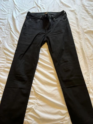 Svarta Lee Scarlett High jeans - Snygga svarta jeans från Lee, modell Scarlett High med hög midja och klassisk femficksdesign. Jeansen har smal passform och dragkedjegylf. Perfekta till en trendig vardagslook och tillverkade i stretchigt material för extra komfort.