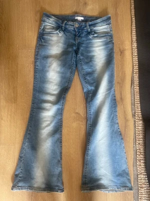 Blå bootcut jeans med slitningar - Snygga blå bootcut jeans med ljusa slitningar framtill och klassisk femficksdesign. Jeansen har låg midja och utsvängda ben, perfekt för en trendig look. Materialet är denim i bomull med lite stretch för extra komfort. Änvädn fåtal gånger .🤗