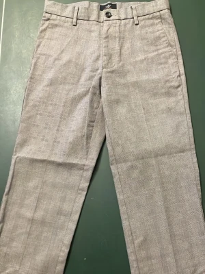 Grå rutiga kostymbyxor dockers  - Snygga grå kostymbyxor från Dockers med diskret rutmönster. Byxorna har raka ben, bälteshällor och bakficka med knapp. Perfekta för en stilren look och passar till skjorta eller t-shirt.