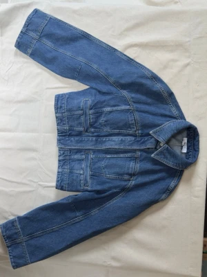 Blå midjekort jeansjacka med dolda knappar - Blå midjekort jeansjacka med breda ärmar och silverfärgade knappar framtill. Använd ett fåtal gånger ✨