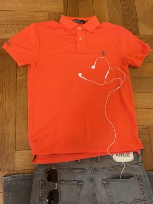 Ralph Lauren piké  - Grym kvalité, inga defekter. Storlek S, sitter bra vid axlarna och slutar vid midjan. Bilderna kan va missledande, färgen är mer rosa än orange, men den är koral färgad.   Mått -|-  Axelmått: 42 cm  Längd: 64 cm  Bröst: 46 cm   Leverans sker dagen efter, har du nån fråga är det bara att skriva:)