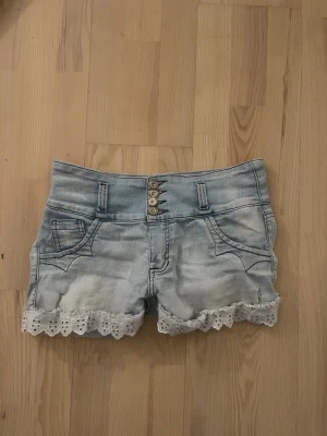 Ljusblå jeansshorts med spetsdetaljer - Jag tror de är omsydda jeans. Säljer ett par ljusblå jeansshorts från leandrus med snygga spetsdetaljer längs bensluten och bakfickorna. Shortsen har fyra knappar framtill, bälteshällor och klassiska fickor både fram och bak. Perfekta för varma dagar!