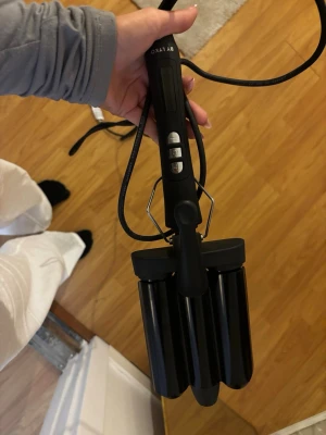 Svart vågtång från BY LYKO - Säljer en svart vågtång från BY LYKO med tre stora värmecylindrar och digitala knappar på handtaget. Perfekt för att skapa snygga beach waves. Handtaget är matt och har metallstöd för att ställa ner tången säkert. Sladd medföljer.