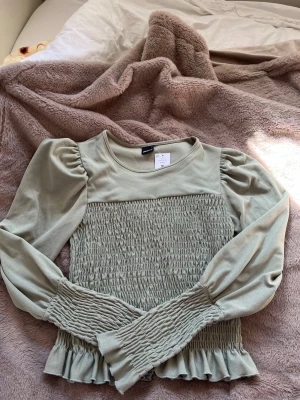 Grön topp från Gina Tricot -  ljusgrön topp från Gina Tricot med puffärmar och volangkant nedtill. Storlek M men passar som S också