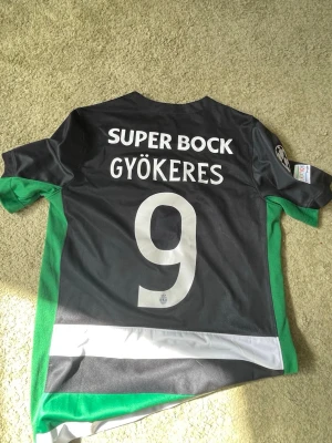 Sporting Lissabon matchtröja Nike - Säljer en officiell Sporting Lissabon matchtröja från Nike med Gyökeres och nummer 9 på ryggen. Tröjan har gröna, vita och svarta ränder, korta ärmar och klubbmärke på bröstet. Materialet är lätt och andas, perfekt för fotbollsträning eller match.