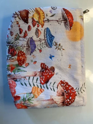 Necessär med svampmotiv - Necessär i tyg med färgglatt svampmönster i rött, blått, gult och lila på ljus bakgrund. Dragkedja upptill och mjuk, rektangulär form. 