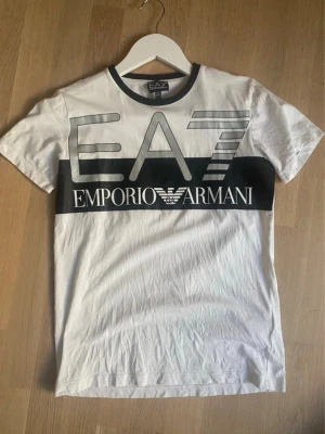 Vit EA7 Emporio Armani t-shirt - Snygg vit t-shirt från Emporio Armani.  Storlek: 166 cm vilket bör motsvara XS för herr Material: 100 % bomull