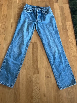 Blå raka jeans i klassisk modell - Säljer ett par blå jeansfrån ASOS  med rak passform och hög midja. Jeansen har fem fickor och stängs med dragkedja och knapp. Tillverkade i klassisk denim, perfekta för en avslappnad och tidlös stil. Storlek 26/32