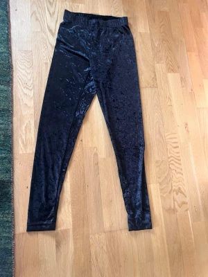 Svarta sammetsleggings - Snygga svarta leggings i glansigt sammetsmaterial med hög midja och smal passform. Perfekta för dig som vill ha en trendig och bekväm look. Materialet är mjukt och stretchigt för extra komfort. Nya med prislapp 