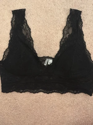 Svart spetsbralette - Säljer en svart bralette i mjuk spets med breda axelband och vacker scallop-kant. Braletten har triangelformade kupor utan bygel och är tillverkad i ett stretchigt spetsmaterial som ger en feminin look. Köpt för 450. Pris kan alltid diskuteras