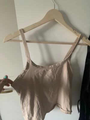 Beige linnetopp från Divided - Snygg beige linnetopp från Divided med smala axelband och enkel design. Toppen är croppad och tillverkad i mjuk bomull, perfekt för varma dagar eller att styla lager på lager.