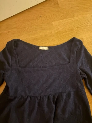 Marinblå spetsblus från Nelly - Snygg marinblå blus från Nelly i storlek M. Blusen har lång ärm, fyrkantig ringning och är gjord i ett spetsliknande material med diskret mönster. Perfekt för dig som gillar en stilren men ändå detaljrik look.