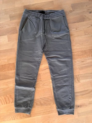 Gråa mjukisbyxor från Prada  - Snygga grå mjukisbyxor från Prada med resår i midjan och muddar vid bensluten. Byxorna har två sidofickor och en bakficka Prada. Perfekta för en chill och avslappnad stil. Tillverkade i mjukt material för extra komfort.