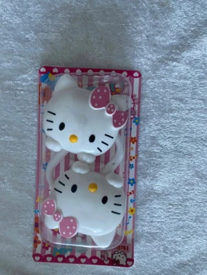 Hello Kitty hårspännen med rosett - Säljer två söta hårspännen i form av Hello Kittys ansikte med vita detaljer och rosa prickiga rosetter. Perfekt accessoar för att piffa upp frisyren med en lekfull och gullig touch. Kommer i originalförpackning med färgglad bakgrund.