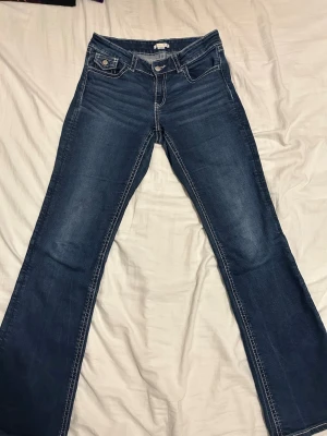 Low waist bootcut jeans från Gina Tricot  - Snygga mörkblå bootcut jeans med vita kontrastsömmar och klassiska fickor både fram och bak. Jeansen har låg midja och är tillverkade i stretchigt denim för en bekväm passform. Perfekta för dig som gillar en tidlös och trendig look. Från Young linjen på Gina Tricot. Köpta för 399kr