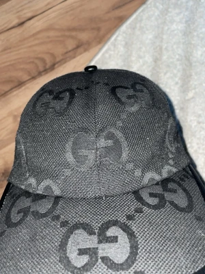 Svart keps från Gucci med GG-mönster - Snygg svart keps från Gucci med det klassiska GG-monogrammet över hela tyget. Kepsen har justerbart spänne bak i svart läder och är tillverkad i ett tåligt tygmaterial. Perfekt för dig som vill ha en stilren accessoar med lyxig känsla.