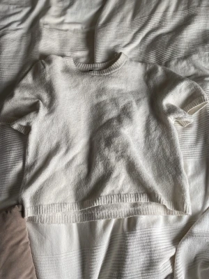 Vit stickad t-shirt i ullmix - Kortärmad stickad t-shirt i mjuk vit ullmix med rund halsringning och ribbade kanter. Perfekt för lager-på-lager och ger en clean, minimalistisk look.