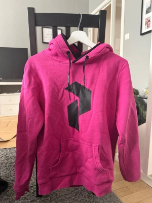 Rosa hoodie med svart tryck - Snygg rosa peak performance hoodie med svart grafiskt tryck på bröstet.