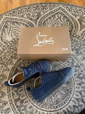 Marinblå sneakers Christian Louboutin - Snygga marinblå sneakers från Christian Louboutin i mocka med matchande blå skosnören och svart sula. Klassisk låg modell med diskret logga på hälen och lyxig känsla tack vare läderdetaljer på insidan. Perfekta för dig som vill ha något exklusivt och stilrent.