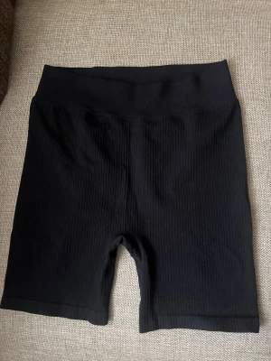 Svarta ribbade cykelshorts - Svarta cykelshorts med ribbad struktur och bred resår i midjan. Perfekta för en sportig look eller till vardagsoutfiten. Mjukt och stretchigt material som sitter skönt på kroppen. Pris går o diskutera 💞