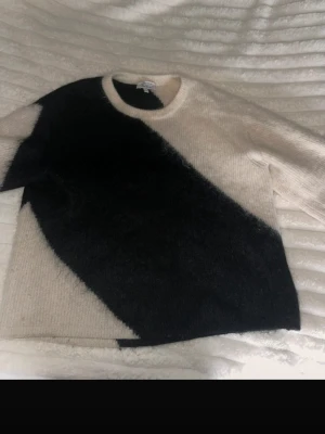 Stickad tröja med svartvit diagonal - Säljer en stickad tröja i mjuk ullmix med bred diagonal färgblock i svart och vitt. Tröjan har rund halsringning och långa ärmar. Inge defekter mer än att den har blivit lite tunnare i materialet vid armbågarna.