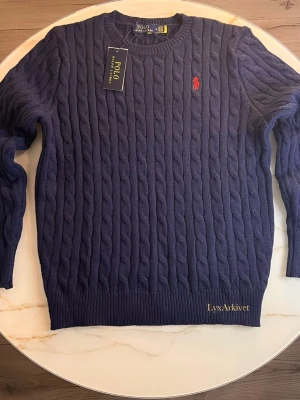 Polo Ralph Lauren Mörkblå kabelstickad tröja - Klassisk kabelstickad tröja från Polo Ralph Lauren i marinblå färg. Mjuk och bekväm kvalitet med rund halsen. Passar grisch stilen                                                                         Storlek M                                                               Skick 10/10 