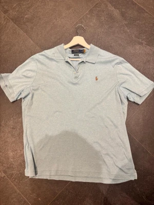 Ljusblå pikétröja från Ralph Lauren - Säljer en klassisk ljusblå pikétröja från Ralph Lauren med den ikoniska broderade loggan på bröstet. Tröjan har krage, knappar framtill och korta ärmar. Perfekt för en clean och stilren look.