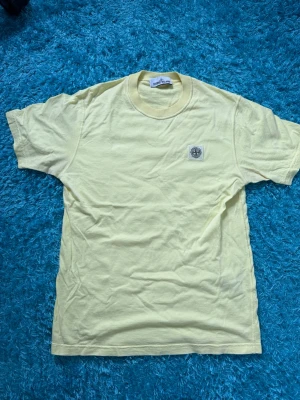 Stone Island - Snygg ljusgul t-shirt från Stone Island med klassisk logopatch på bröstet. T-shirten har rund halsringning och korta ärmar. Tillverkad i mjuk bomull som känns skön mot huden. Storlek S, helt oanvänd. Hör gärna av er vid frågor/funderingar.