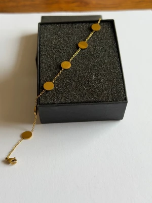 Guldigt fotlänk med runda plattor - Snyggt fotlänk i  guldfärgad metall med flera runda, blanka plattor längs en tunn kedja. Perfekt accessoar för att lyfta din stil med en modern och minimalistisk touch. Justerbar längd med smidig karbinhake.