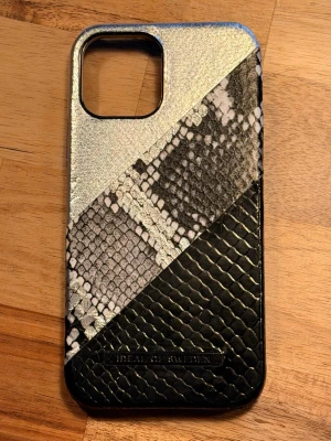 Mobilskal i ormmönster från iDeal of Sweden - Snyggt mobilskal med metallic, svart och grått ormmönster från iDeal of Sweden. Skalet har en lyxig känsla med olika texturer och passar perfekt för dig som vill ha något unikt till mobilen. Tillverkat i konstläder med präglad yta och öppning för kamera.