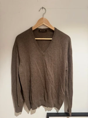 Loro Piana V-ringad stickad tröja - En klassisk brun stickad tröja med V-ringning och långa ärmar. Tröjan har ribbstickade muddar vid ärmslut och nederkant. Perfekt för lager-på-lager och enkel att matcha med olika outfits.