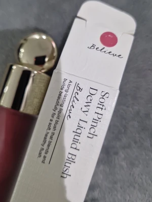 Rare Beauty Soft Pinch Dewy Liquid Blush - Rare Beauty Soft Pinch Dewy Liquid Blush i nyansen Believe. Flytande rouge med en mjuk, rosa-lila ton som ger en fräsch och naturlig glow. Kommer i en stilren glasflaska med guldfärgat lock och applikator. Perfekt för att bygga upp färg och lyster.