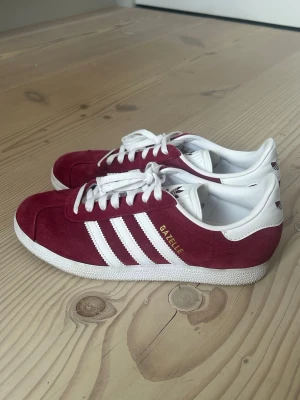 Vinröda Adidas Gazelle - Säljer dessa röda adidas gazelles då jag har köpt ett par andra skor. Strl 39 1/3 och har använts ca 10 gånger. Finns spår av användning. Nypris 1349kr!