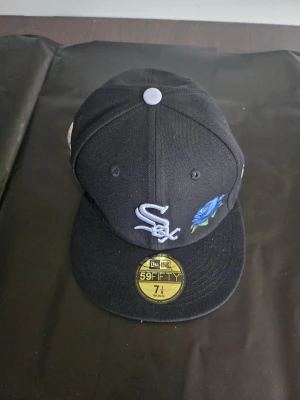 Svart White Sox keps New Era 59FIFTY - Svart keps från New Era 59FIFTY med broderad White Sox-logga framtill och en blå ros. Sidan har ett broderat jubileumsmärke för White Sox 95 år (1901-1995). Klassisk flat peak och vit knapp på toppen.