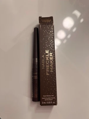  Freckle Maker från märket Nabla - Nabla Freckle Maker är en flytande produkt för att skapa naturliga fräknar. Kommer i en brun tub med guldiga detaljer och tillhörande förpackning. Enkel att applicera med smal spets för precision.