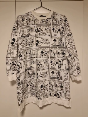 Disney Mickey Mouse comic sweatshirt - Vit oversized sweatshirt med svart serietidningsmönster av Mickey Mouse. Långa ärmar, ribbade muddar och rund halsringning. Trycket täcker hela tröjan och ger en cool retrovibe. Perfekt för dig som gillar streetstyle och Disney.