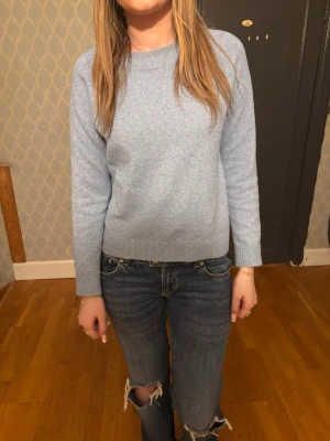 Ljusblå stickad tröja - Mysig ljusblå stickad tröja med rund halsringning och långa ärmar. Tröjan har en enkel och stilren design med ribbade muddar vid ärmslut och nederkant. Perfekt att matcha med jeans för en avslappnad look.