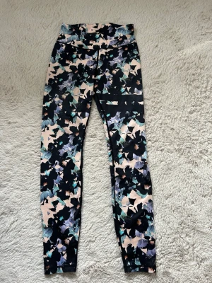 Mönstrade leggings från Stronger - Snygga leggings från Stronger med hög midja och  blommigt mönster i svart, rosa, blått och grönt. Stretchigt material som sitter skönt och följer kroppen. Perfekta för träning.