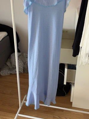 Ljusblå långklänning med volang - Osäker på storlek pga ingen lapp! Snygg ljusblå långklänning med volangdetalj längst ner och offshoulder-design. Klänningen har en luftig och somrig känsla, perfekt för varma dagar. Tillverkad i ett lätt material som ger ett avslappnat intryck.