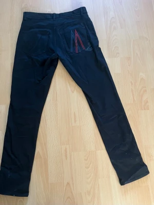     Moncler chinos – röd/blå M-logga - Säljer ett par stilrena Moncler chinos med den ikoniska M-loggan i blått och rött. Byxorna är i nyskick – aldrig använda och endast legat i garderoben. Perfekta för dig som vill ha en clean men exklusiv look. Lite skrynkliga just nu, men det försvinner enkelt vid tvätt eller strykning. Riktigt bra chans att få tag på ett par i toppskick!