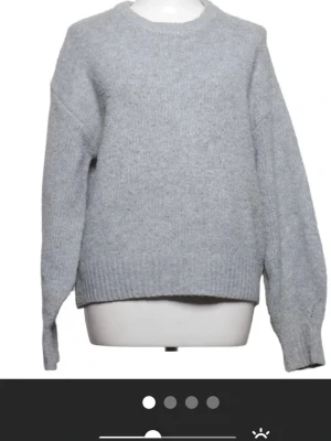 Ljusgrå stickad tröja - En enkel och stilren ljusgrå stickad tröja med rund halsringning och långa ärmar. Tröjan har ribbstickade muddar vid ärmslut och nederkant. Perfekt för lager-på-lager och passar till det mesta.